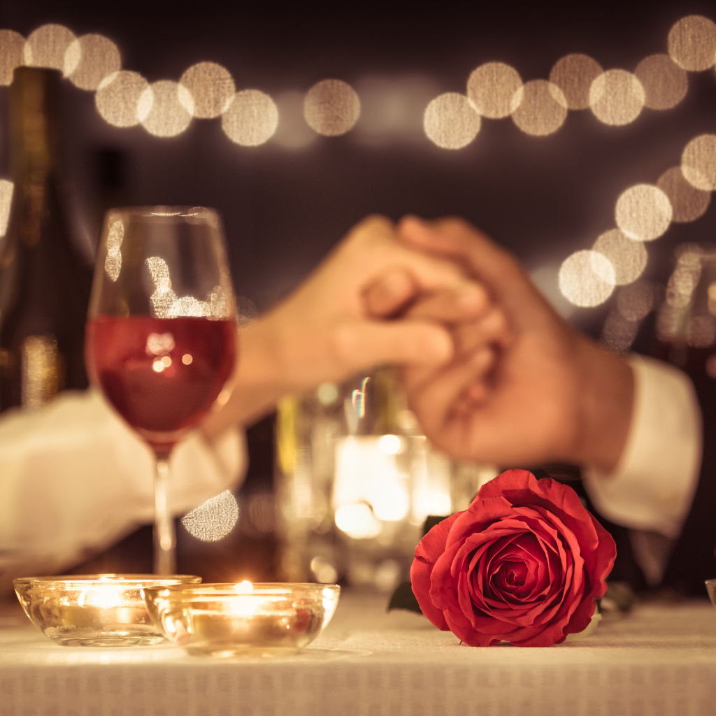 Anniversary-couple-holding-hands-red-rose-and-wine-in-restaurant