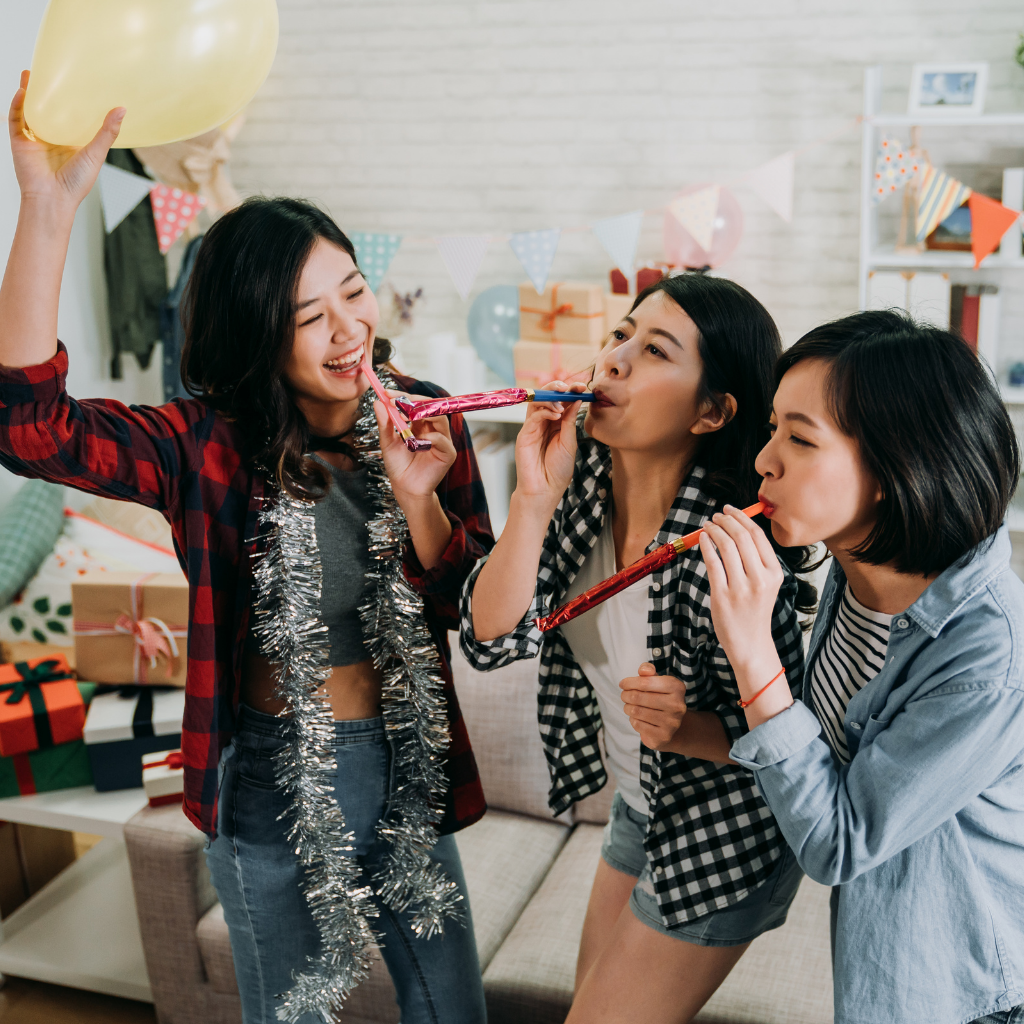 Three women celebrating with party blowers and a balloon at a housewarming party.