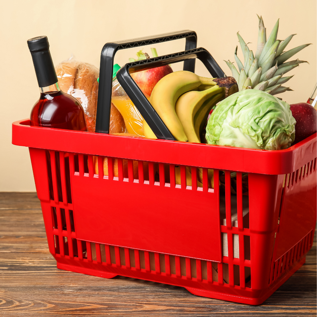 A red shopping basket filled with fresh groceries, bread, and a bottle of wine.