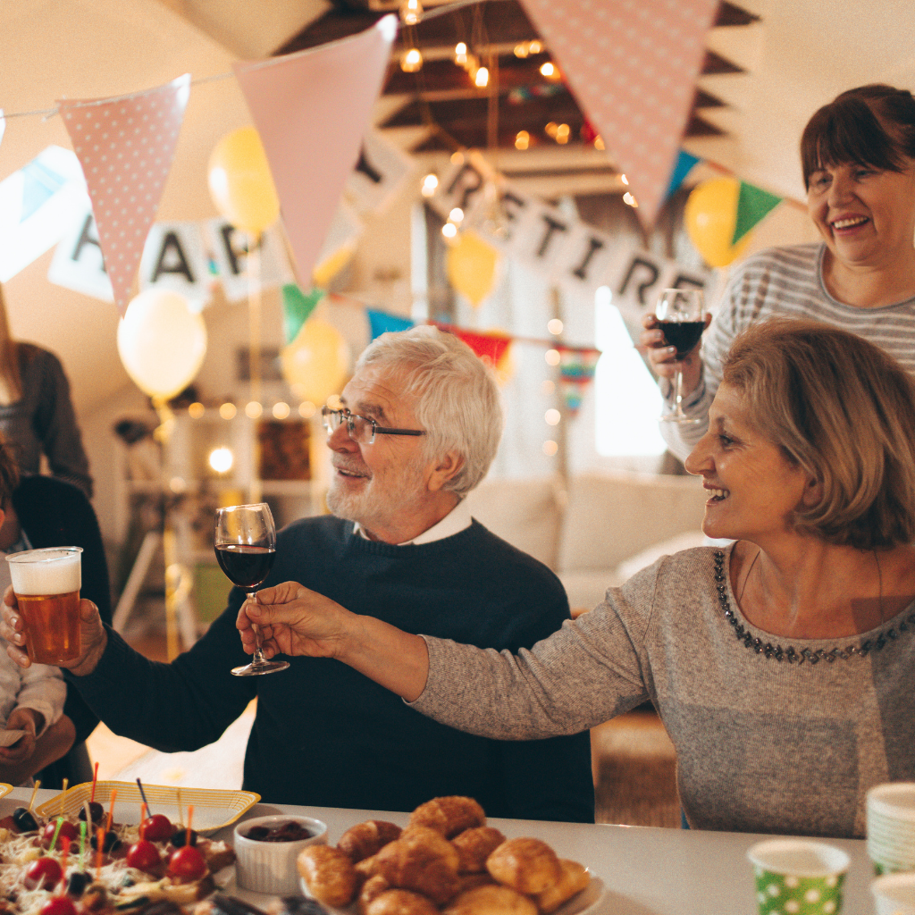 Senior couple toasting with drinks at a retirement party with friends and decorations.