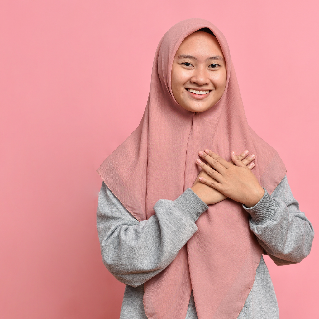  A Muslim Malay woman with a thankful gesture, hands on chest, wearing a hijab.