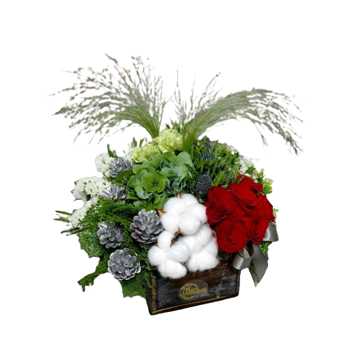 Christmas-themed floral arrangement in a wooden box with red roses, white cotton flowers, pine cones, and a lush mix of greenery and foilage