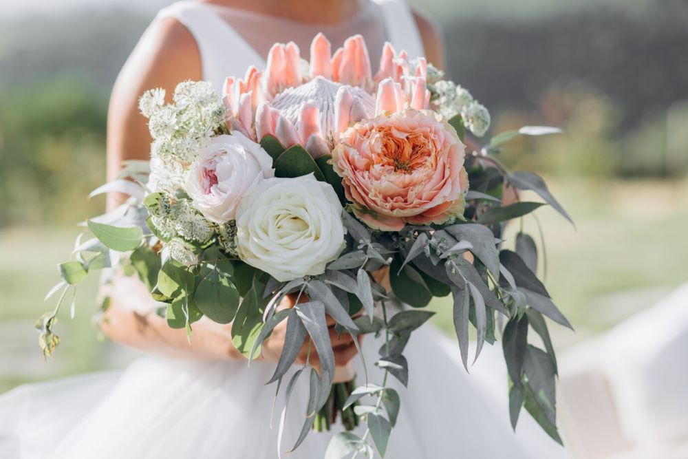 A stunning bridal bouquet composed of peach and white roses, accented with eucalyptus leaves and white filler flowers, held by a bride in a white dress.