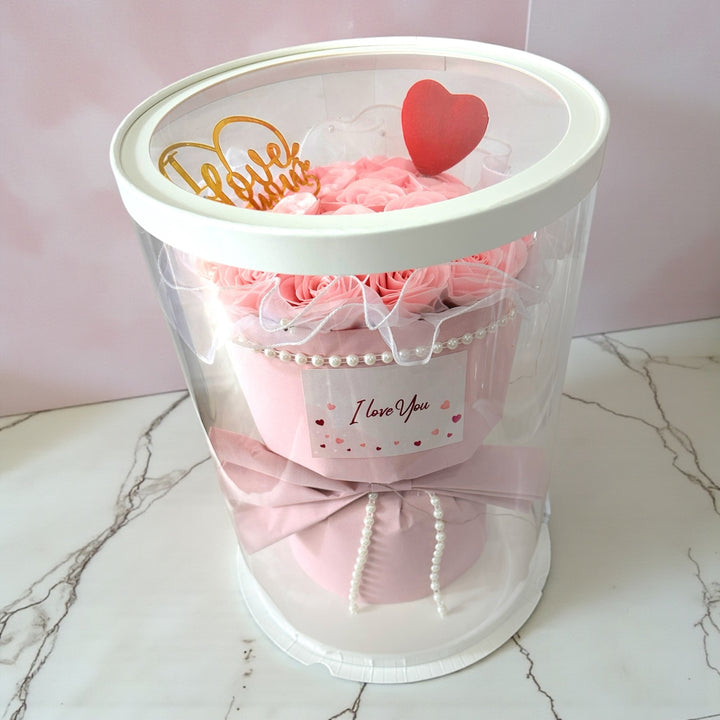 Pink bouquet in a clear container with decorative elements on a marble surface.